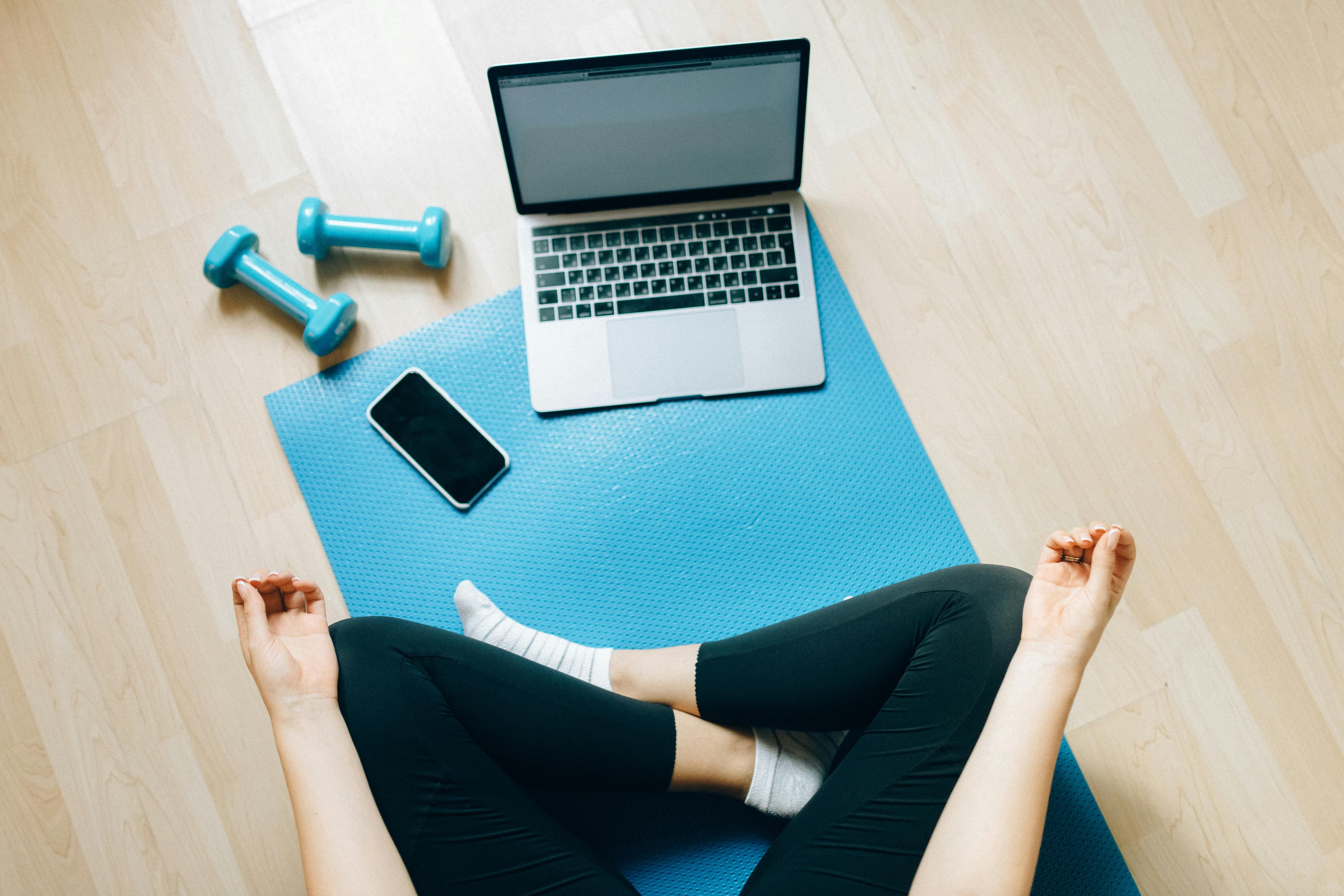 Overhead view of a yoga mat with dumbbells, laptop, and phone ready for a home workout
